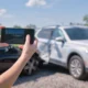 Female taking picture of damaged cars for sale.